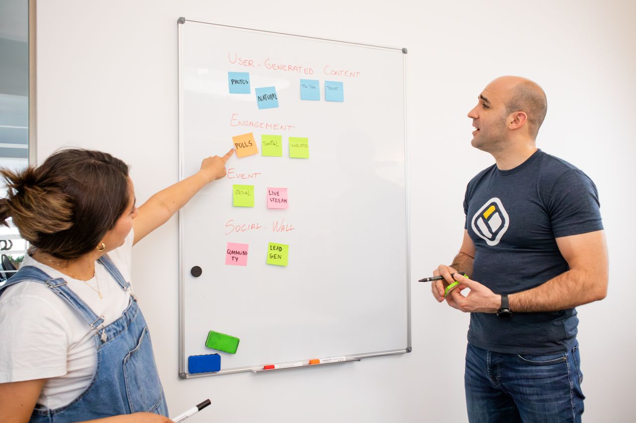 Two colleagues brainstorm on a whiteboard with colorful sticky notes for project planning.